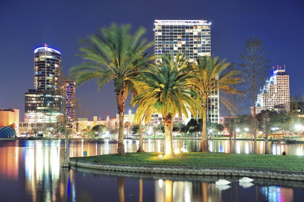 Orlando downtown skyline panorama over Lake Eola at night with urban skyscrapers, tropic palm tree and clear sky.