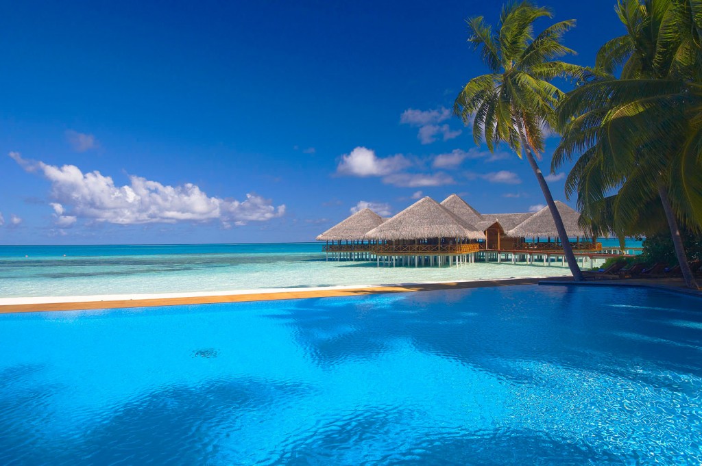 Een blauwe oceaan en luxe huisjes op palen in het water